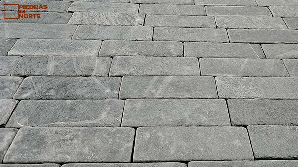 Adoquín de pizarra suavizada en acceso de vivienda moderna.